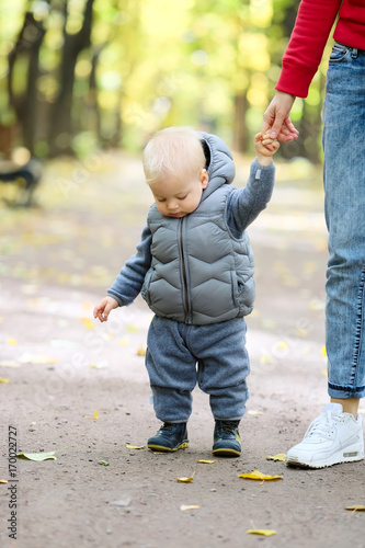One year old baby boy in autumn park learning to walk with his mother.