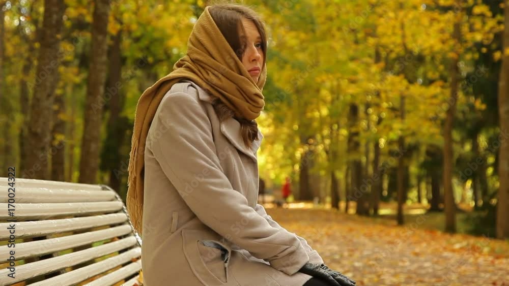 Woman in grey coat and scarf. She sitting on a bench and waiting for someone Woman in grey coat and scarf. She sitting on a bench and waiting for someone