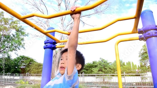 Slow motion of young asian Thai boy hang the yellow bar by his hand to exercise at the outdoor playground during the summer sunlight.