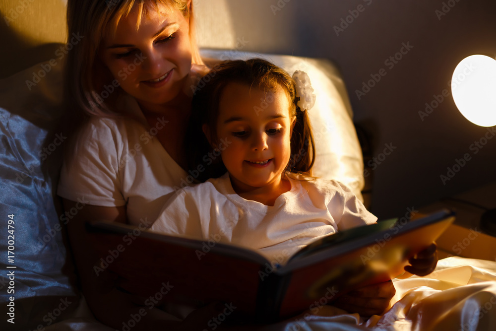 mother and child girl reading a book in bed before going to sleep mother and child girl reading a book in bed before going to sleep