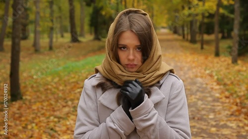 Beautiful sad caucasian woman in grey coat and knitted scarf in park at autumn