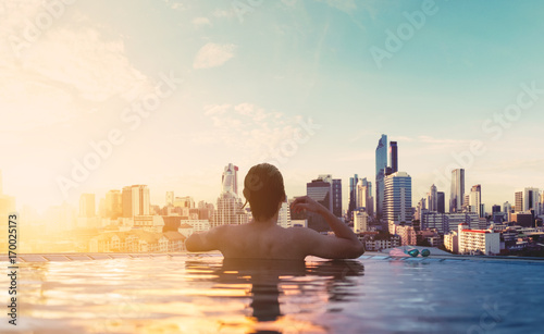 a man relax in swimming pool in sunrise, on rooftop in the city