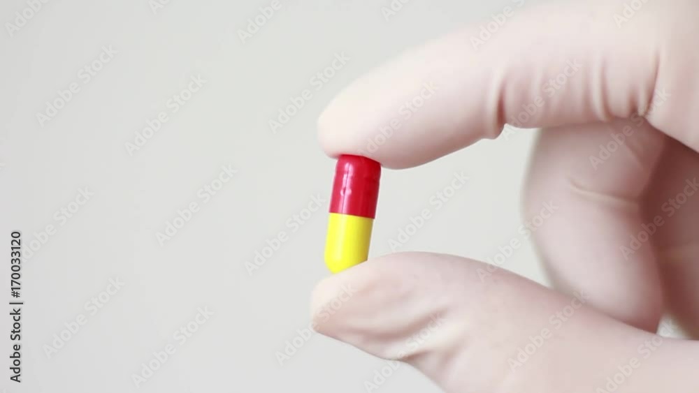 Holding yellow-red pill in rubber gloves Holding yellow-red pill in rubber gloves