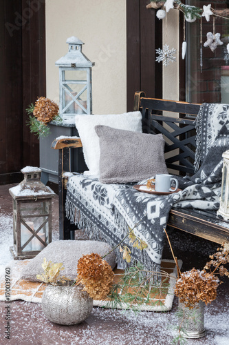 Vintage blanket on wooden bench with pillows, candlesticks, cup of coffee. Rustic style. Cozy plaid lie on snowed chair. New year decorations. Winter Christmas background.