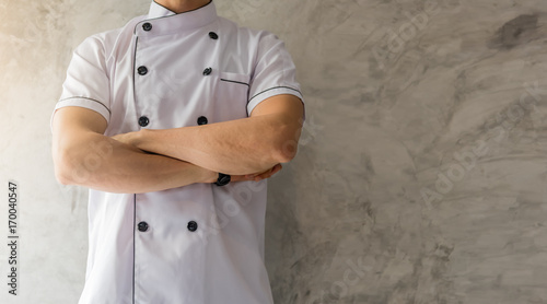 Fototapeta Naklejka Na Ścianę i Meble -  Handsome caucasian man professional Chef arms crossed in white uniform on gray cement wall with copyspace