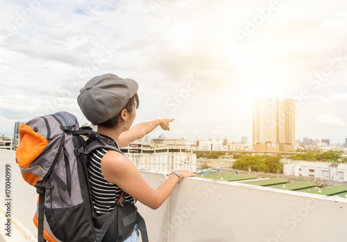 Back view of cheerful young backpack happiness asian woman with hands up on city view. Freedom traveler concept.with copy space