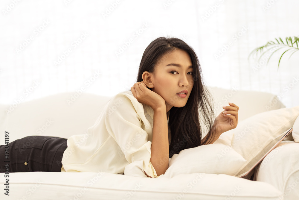 Young asian businesswoman lying on sofa with tablet computer in her hands at home in morning time. Young asian businesswoman lying on sofa with tablet computer in her hands at home in morning time.