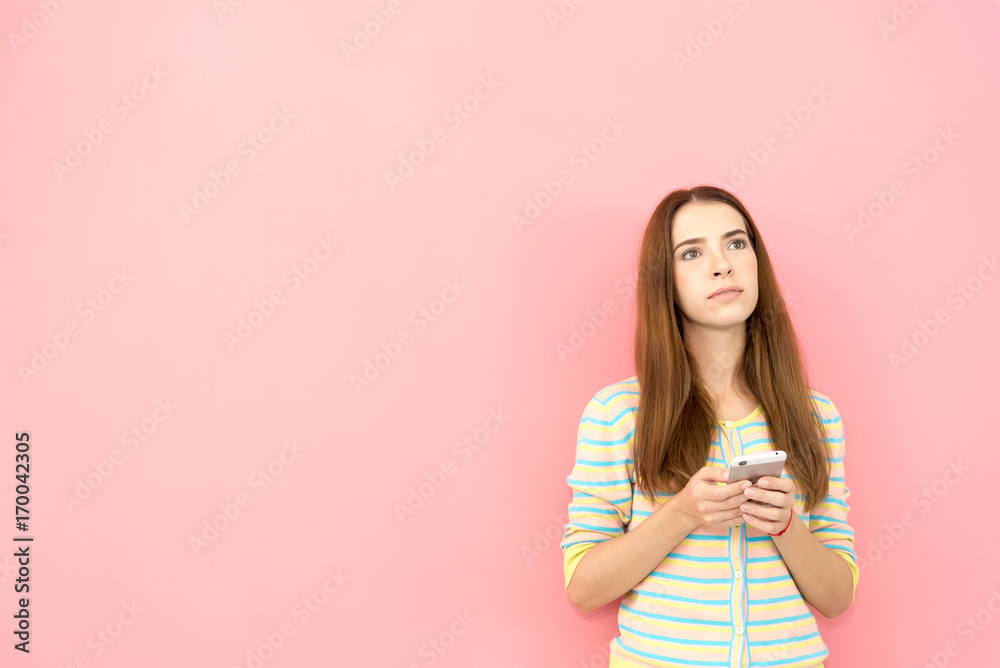 Portrait of caucasian attractive beautiful Smiling young woman thinking while using smart phone in hands isolated on pink wall with copy space,half body Portrait of caucasian attractive beautiful Smiling young woman thinking while using smart phone in hands isolated on pink wall with copy space,half body
