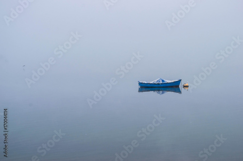 Boat on calm late water in a foggy morning