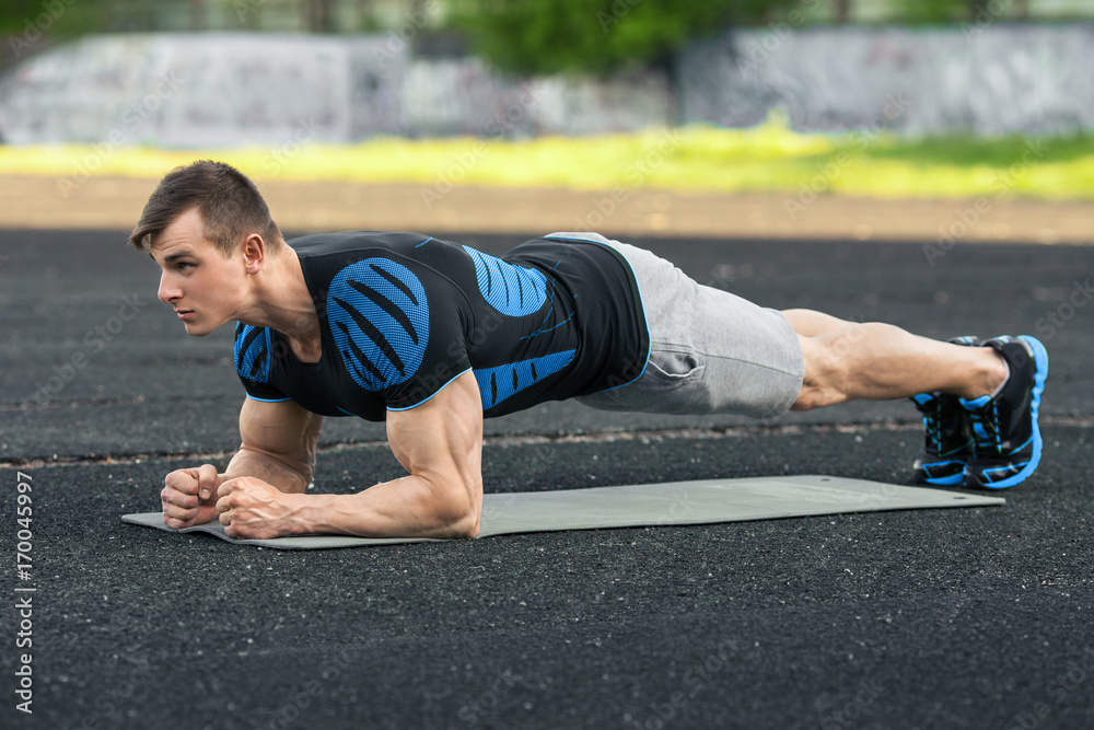 Active fitness man doing planking exercise in the stadium, muscular male workout, outdoors. Active fitness man doing planking exercise in the stadium, muscular male workout, outdoors.