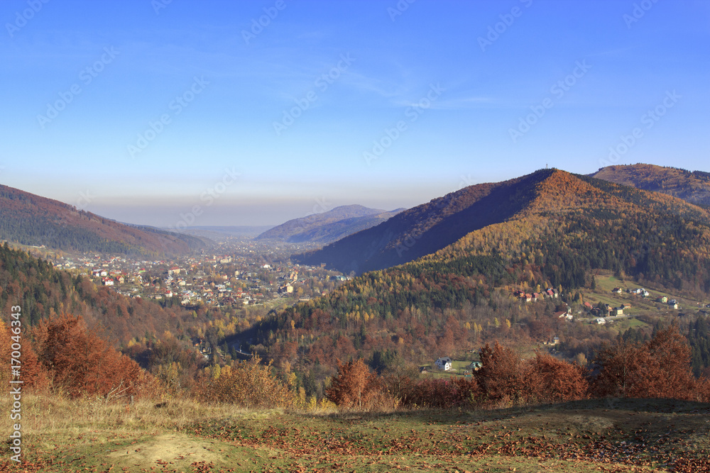 Autumn landscape in Carpathian lowlands with colorful forests and a village in a valley