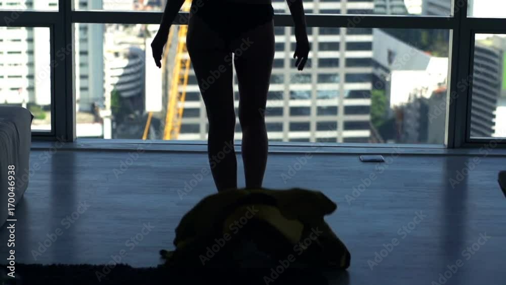 Woman taking off dress, walking towards window at home
