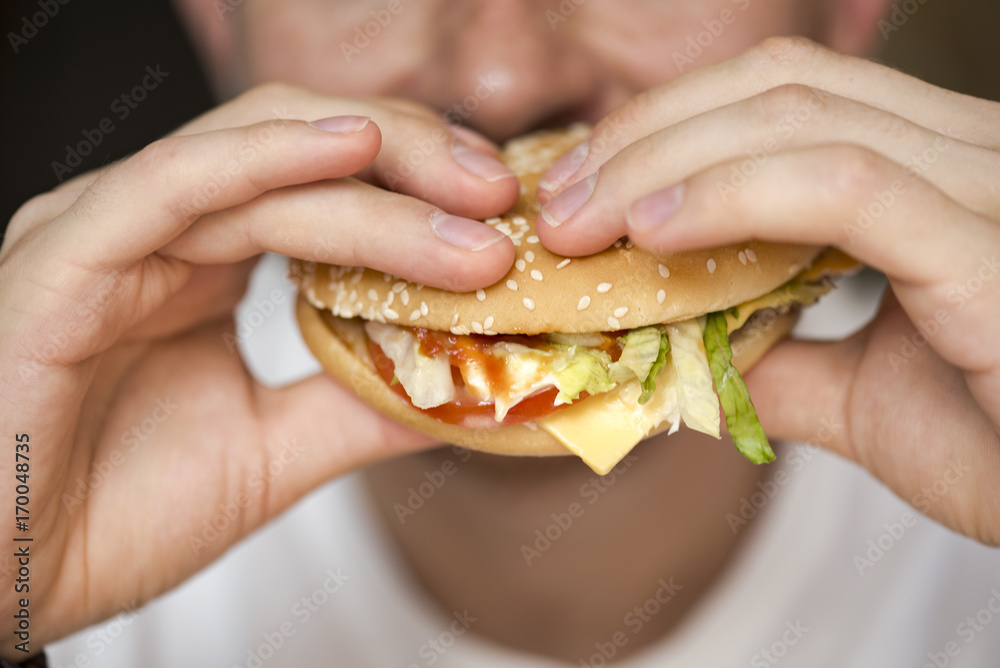 Man eating hamburger with vegetables at a fast food restaurant, fast food knowns like unhealthy food in the world