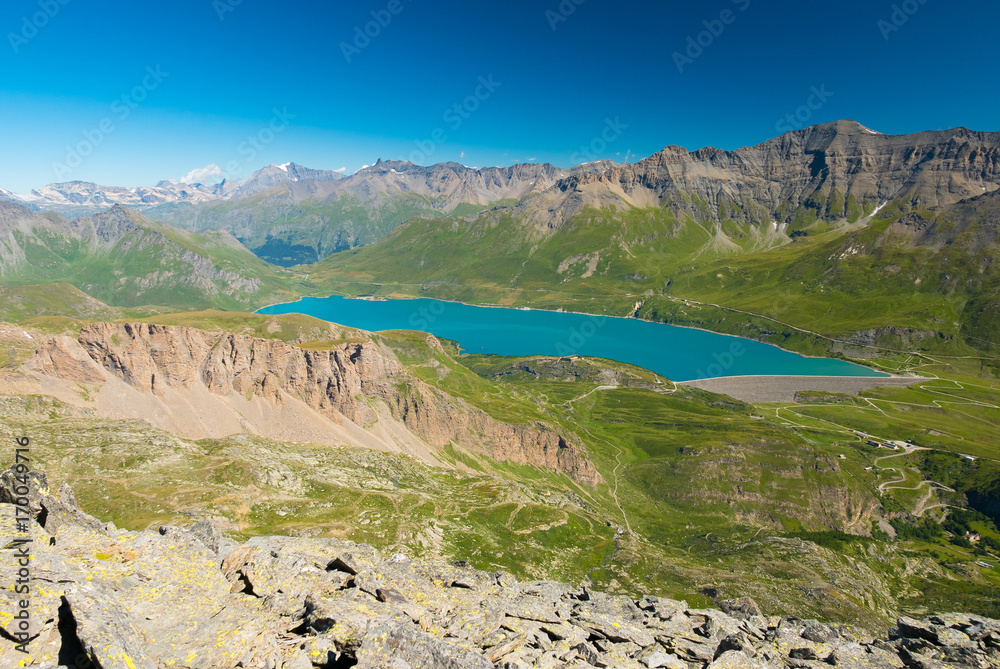 High altitude blue lake, dam on the Italian French Alps. Expansive view from above, clear blue sky.