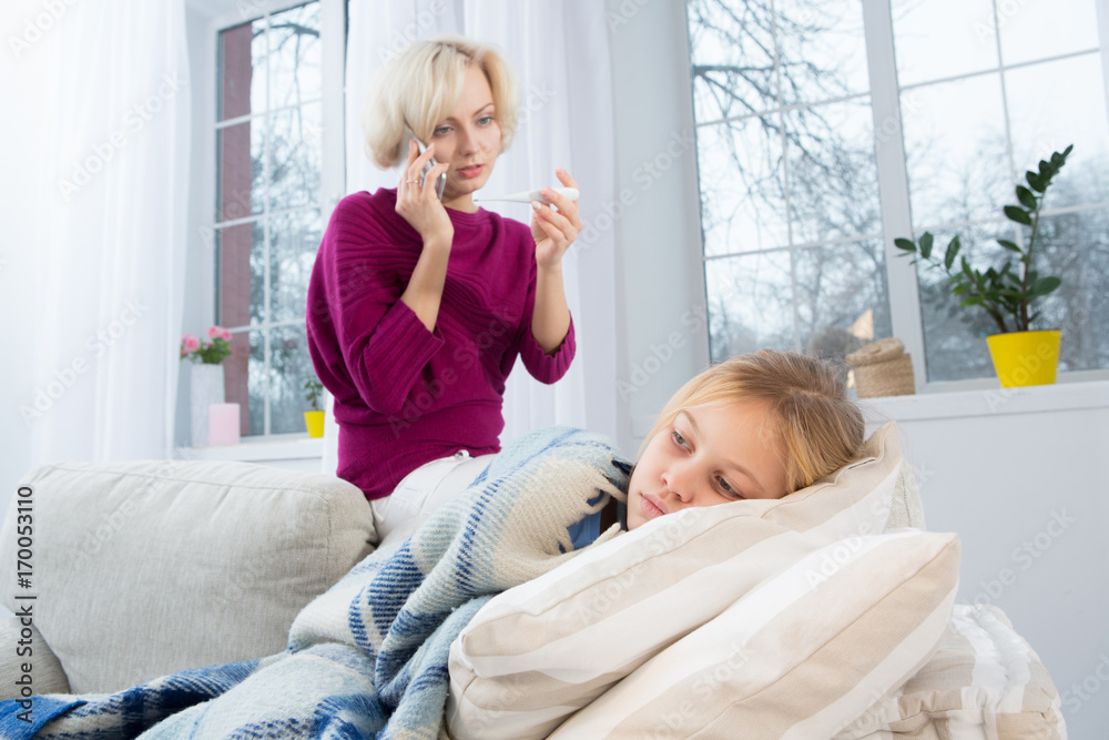 Mother measuring temperature of her child and calling doctor. Sad mom holding thermometer in one hand and cell phone in another.