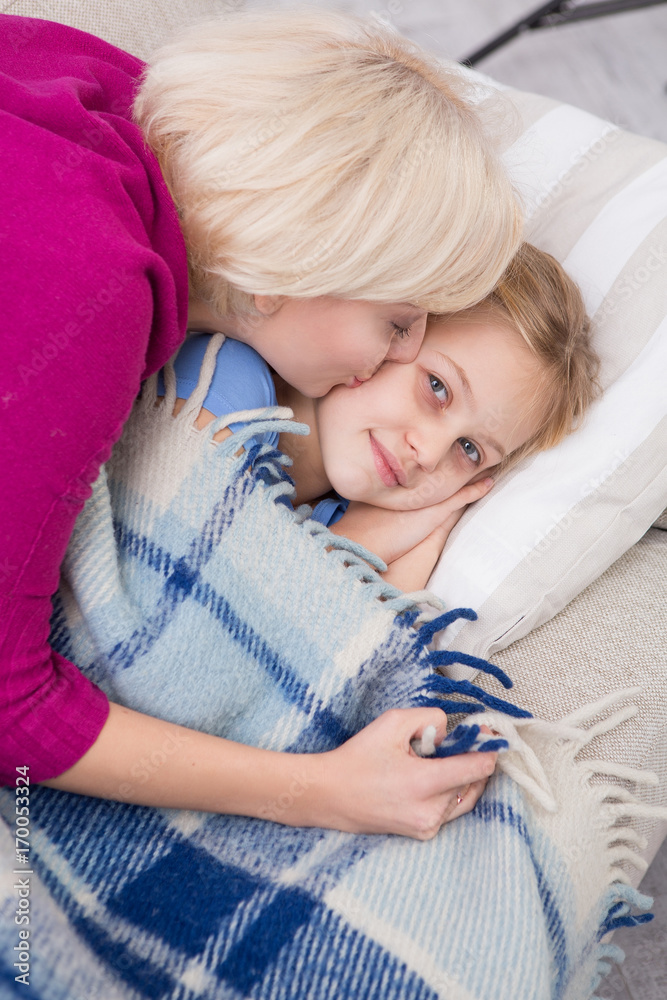 Top view of mother kissing her little sick daughter. Little girl lying on sofa in living room.
