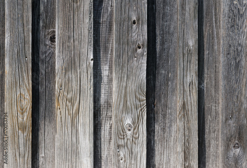 Weathered old wooden wall detail. Simple gray boards with knotholes and coarse grain nailed together. Outdoor. Backgrounds. Photo.