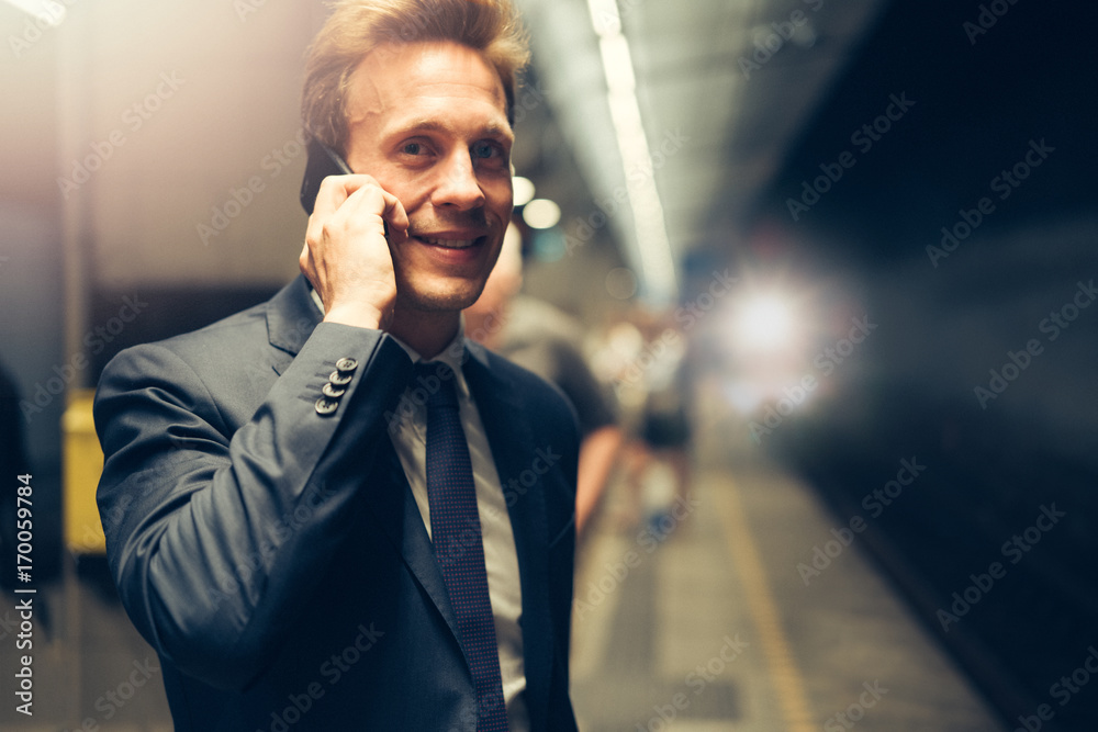 Smiling businessman standing in a subway station reading text me Smiling businessman standing in a subway station reading text me