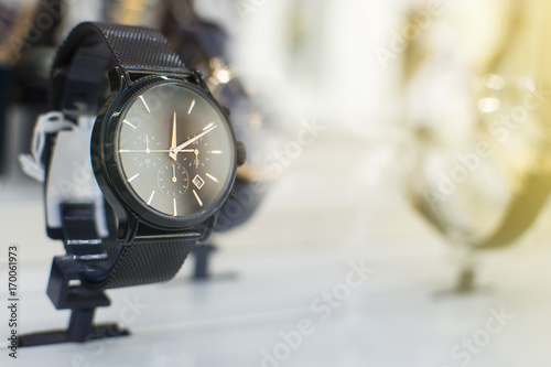 Close up of an beautiful black stainless steel watch. Beautiful watch in front of other watches. Lens flare in background.