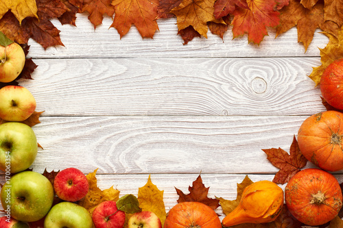 Autumn leaves, apples and pumpkins over wooden background