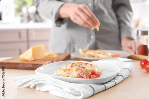 Woman preparing lasagna with cheese on table in kitchen