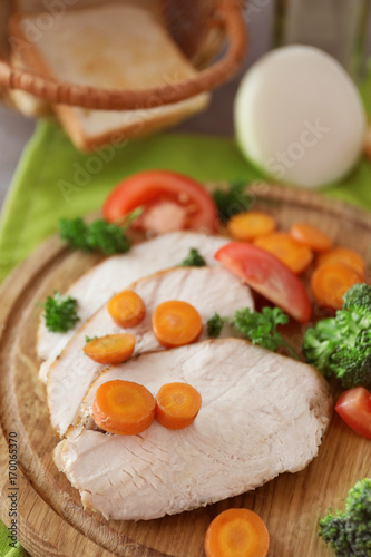 Cutting board with delicious sliced turkey fillet and vegetables on table, closeup