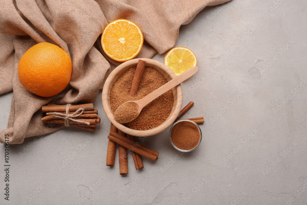 Cinnamon sticks and sugar in wooden bowl with oranges on grey background Cinnamon sticks and sugar in wooden bowl with oranges on grey background