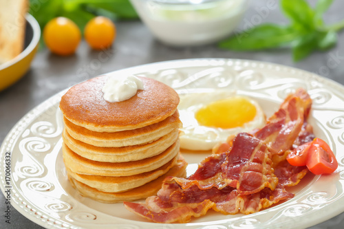 Tasty breakfast with pancakes, fried egg and bacon on table
