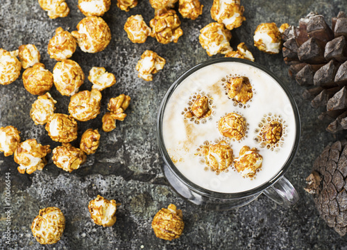 A glass of mouth-watering sweet milk coffee with a creamy foam topped with caramel crispy popcorn on a gray stone background. Selective focus. photo