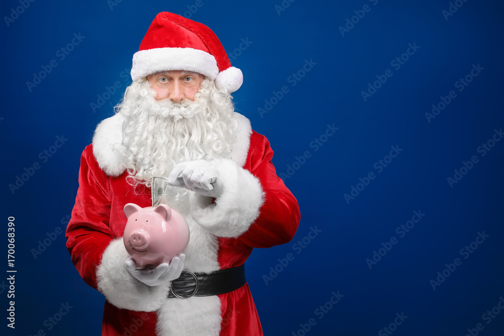 Santa Claus putting dollar into piggy bang on color background Santa Claus putting dollar into piggy bang on color background