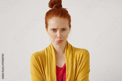 Принти на полотні Unhappy upset red-haired teenage girl with hair knot having offended and dissapointed look, pouting as she has to stay at home being grounded for bad grades at school
