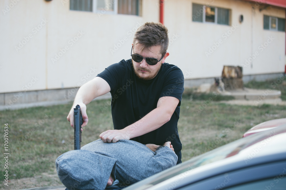 Obraz premium Arrest of thieves, criminals, hands bound with police cuffs, a gun directed at the head, a thief disabled, leaning on the hood of a police car