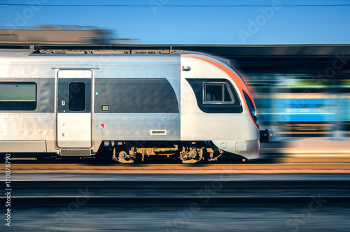 High speed train in motion at the railway station at sunset in Europe. Modern intercity train on the railway platform with motion blur effect. Moving passenger train on railroad. Transportation