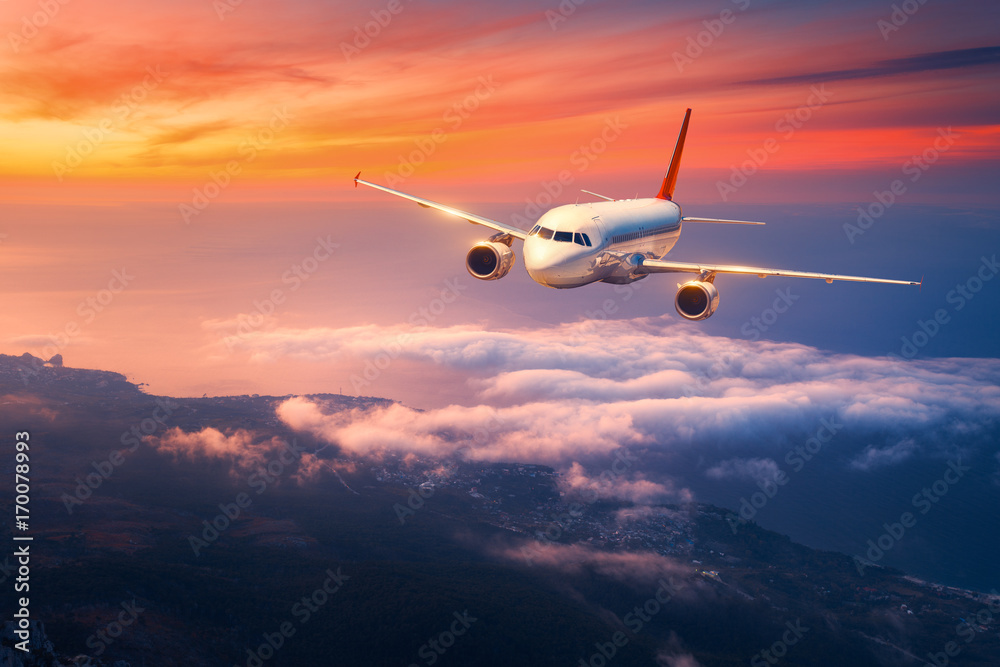 Fototapeta premium Passenger airplane. Landscape with big white airplane is flying in the sky over the clouds and sea at colorful sunset. Passenger aircraft is landing at dusk. Business trip. Commercial plane. Travel