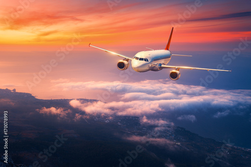 Passenger airplane. Landscape with big white airplane is flying in the sky over the clouds and sea at colorful sunset. Passenger aircraft is landing at dusk. Business trip. Commercial plane. Travel