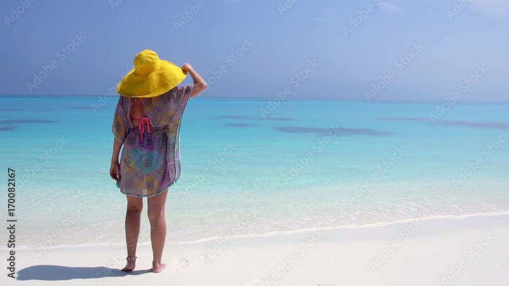 Woman in straw yellow sunhat looking to the sea on sandy beach Woman in straw yellow sunhat looking to the sea on sandy beach