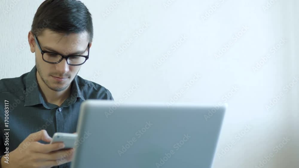 Portrait of a young man wearing glasses sitting in his office in front of a monitor - working on a computer and talking on the phone. People stock footage slider shot. 
