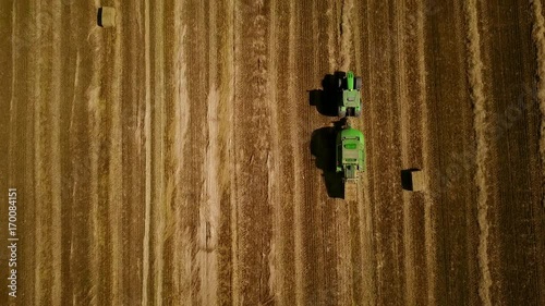 4K. Modern tractor makes haystacks on the field after harvesting. Aerial top view.