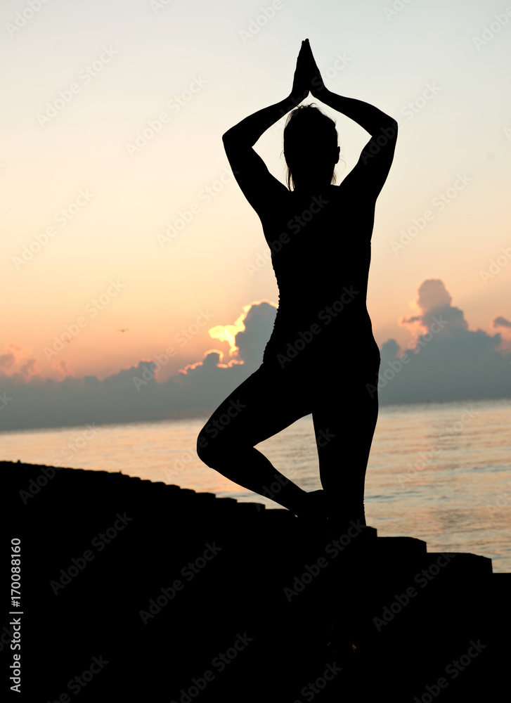 Young active woman practicing yoga on the beach at sunrise