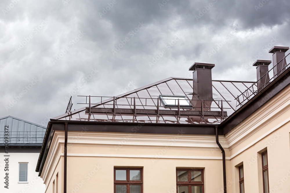house with brown metal wet roof, chimneys and skylights during rain