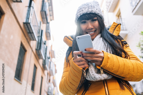 Smiling asian woman using her mobile in european street. photo