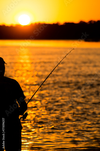 Fisherman with a fishing rod at sunset
