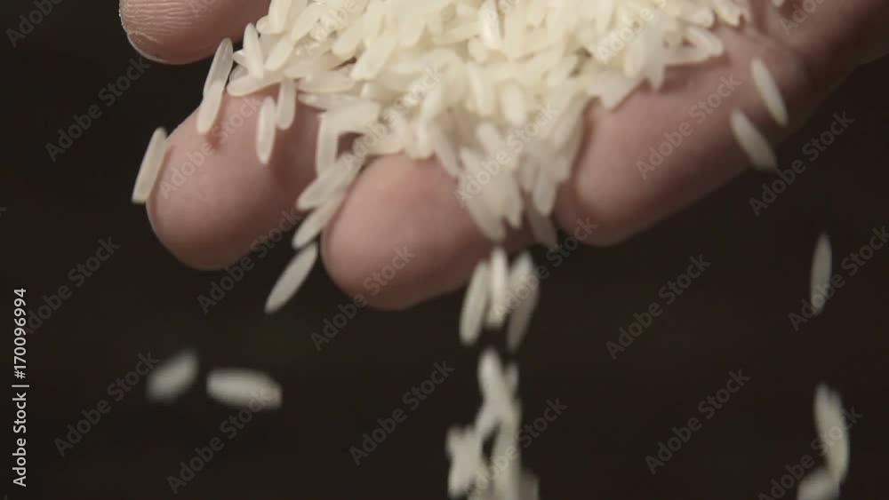 White raw rice grains are falling from a man's hand in slow motion White raw rice grains are falling from a man's hand in slow motion