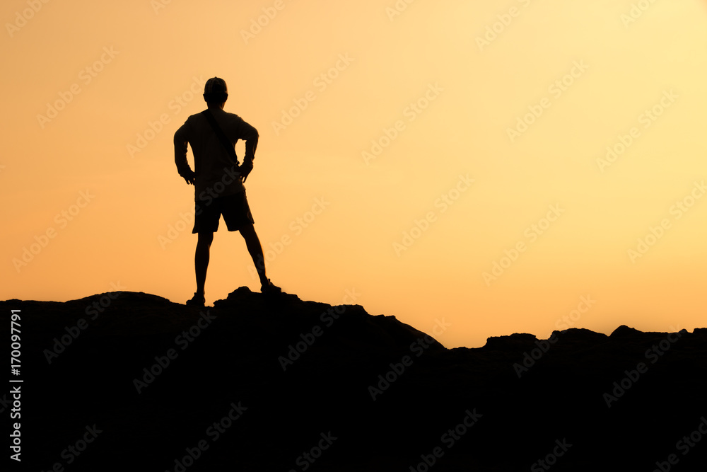 silhouette of man standing on peak of stone and watching sun in the morning.