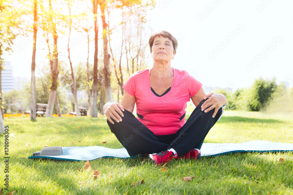 Fototapeta premium Senior woman doing yoga exercise on green grass in the park.