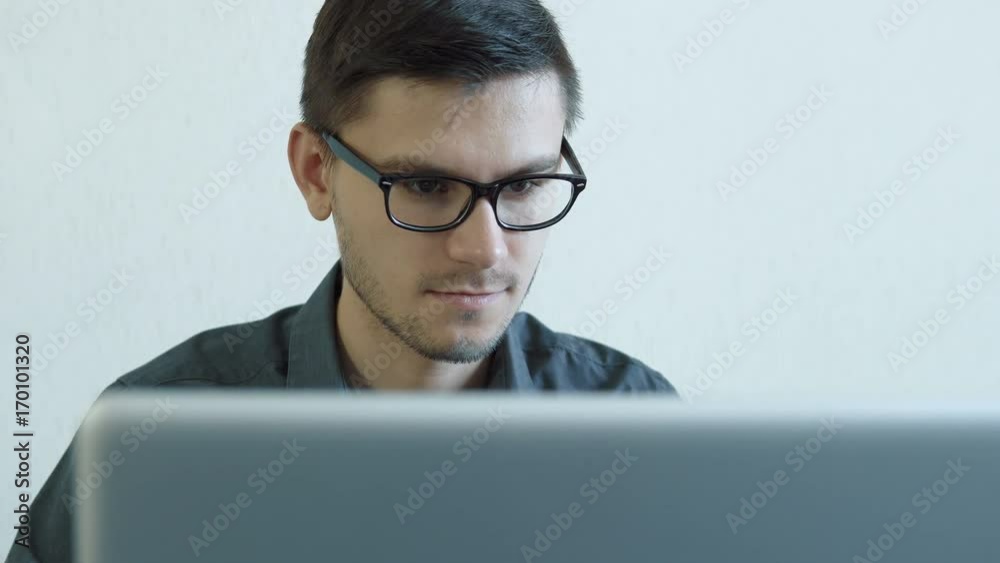 Portrait of a young man wearing glasses sitting in his office in front of a monitor - working on a computer. People stock footage shot. Portrait of a young man wearing glasses sitting in his office in front of a monitor - working on a computer. People stock footage shot.
