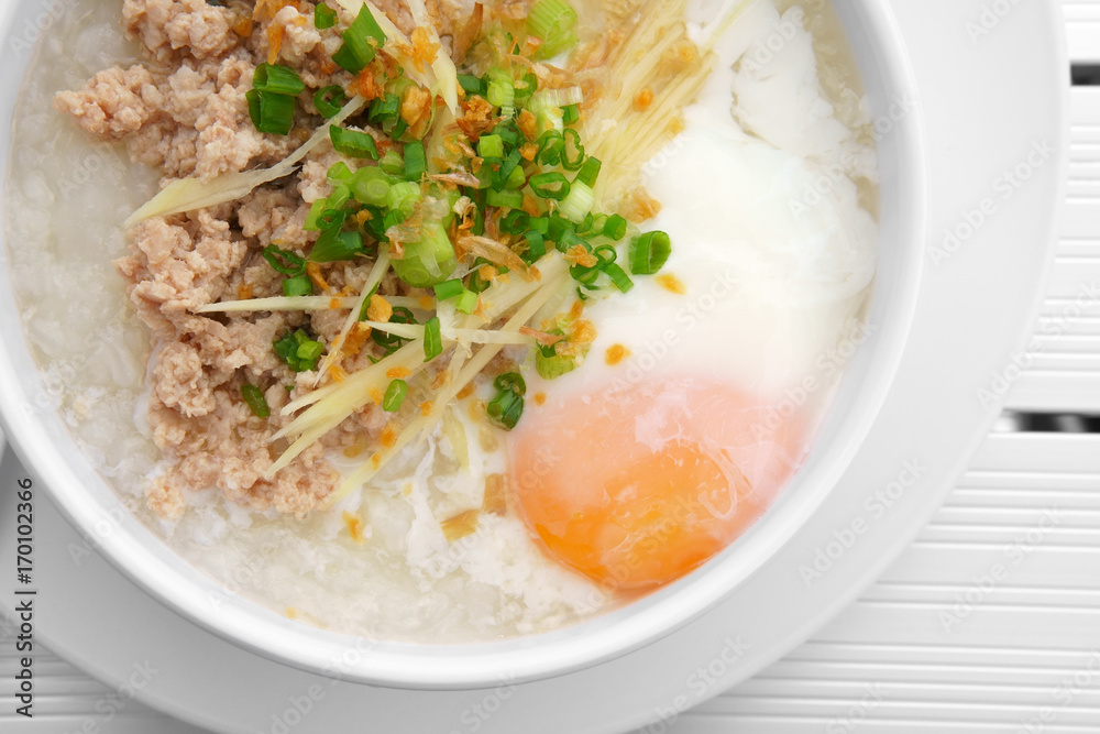 pork chops rice porridge or congee with soft boiled egg and vegetable in the white bowl with spoon on the top view aluminium and white table for delicious breakfast and clean food in the morning pork chops rice porridge or congee with soft boiled egg and vegetable in the white bowl with spoon on the top view aluminium and white table for delicious breakfast and clean food in the morning