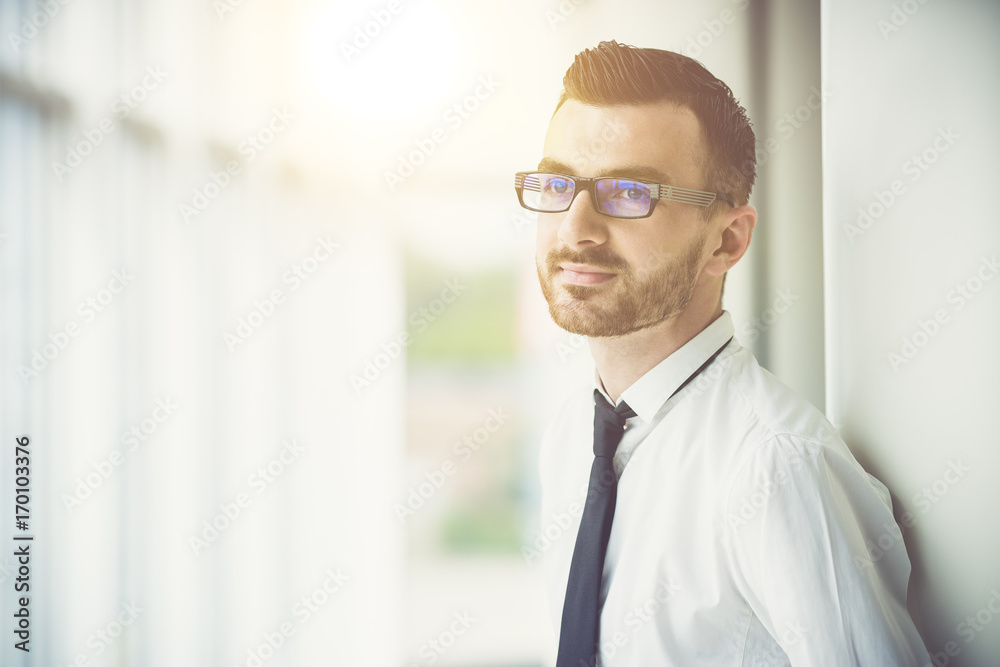 The man in glasses stand near the column in the office on the sun background The man in glasses stand near the column in the office on the sun background
