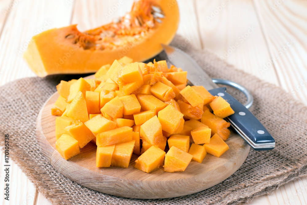Cubes of pumpkin on cutting board and knife on wooden table Cubes of pumpkin on cutting board and knife on wooden table