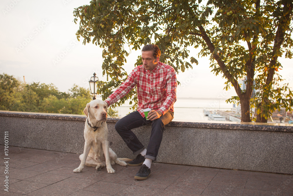 Young men relaxing in the mornin city with cup of coffee or tea and labrdor dog Young men relaxing in the mornin city with cup of coffee or tea and labrdor dog